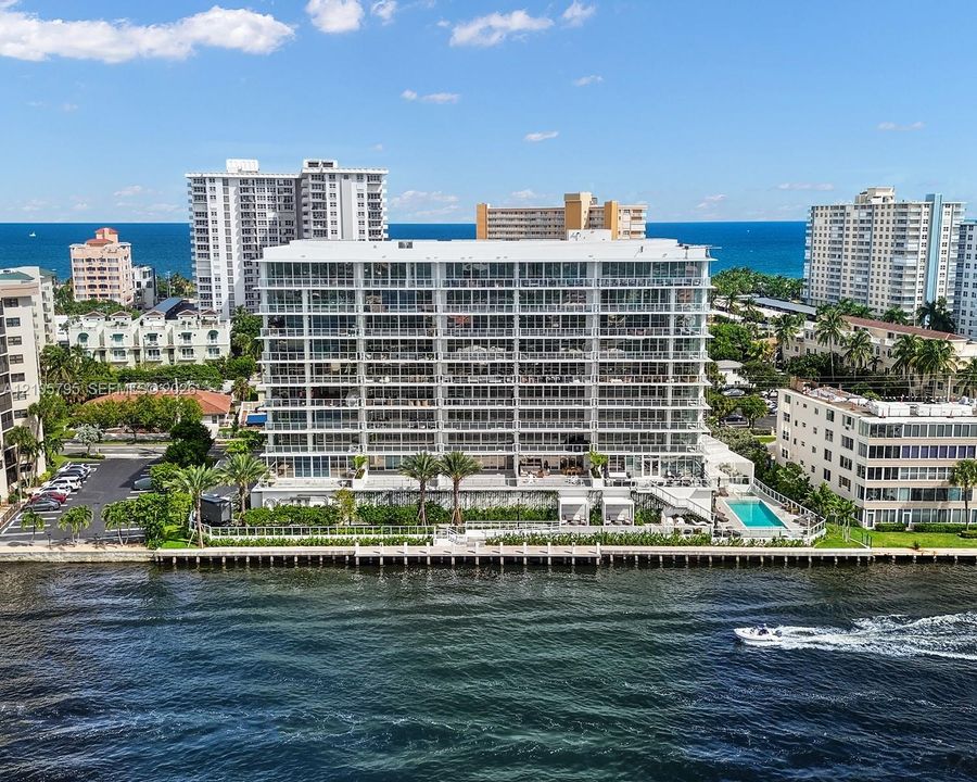 Waterfront multi-story residential building featuring floor-to-ceiling glass balconies, private dockage, a ground-level swimming pool, and manicured landscaping