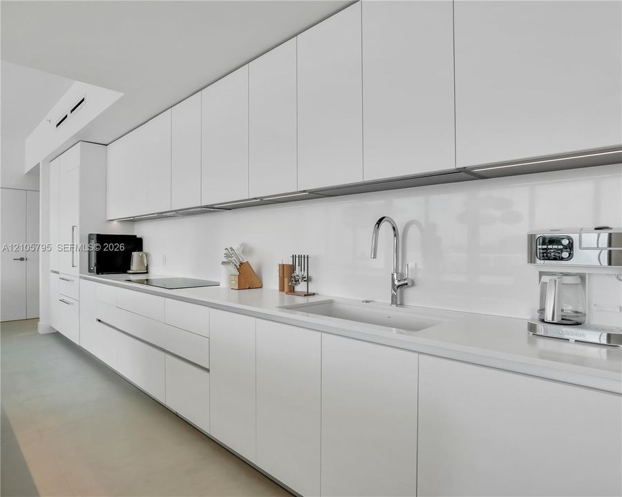 Minimalist kitchen featuring flat-panel cabinetry, solid-surface countertops, a seamless backsplash, an integrated induction cooktop, and a chrome gooseneck faucet