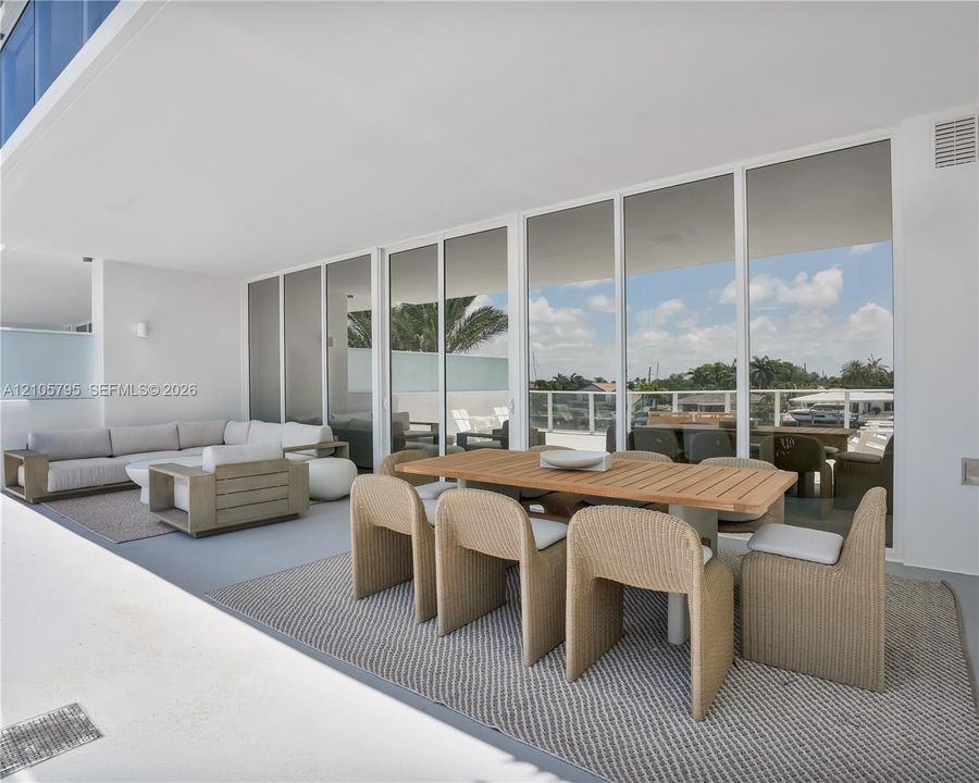 Expansive covered terrace featuring floor-to-ceiling glass wall panels, smooth concrete flooring, and an attached white railing system