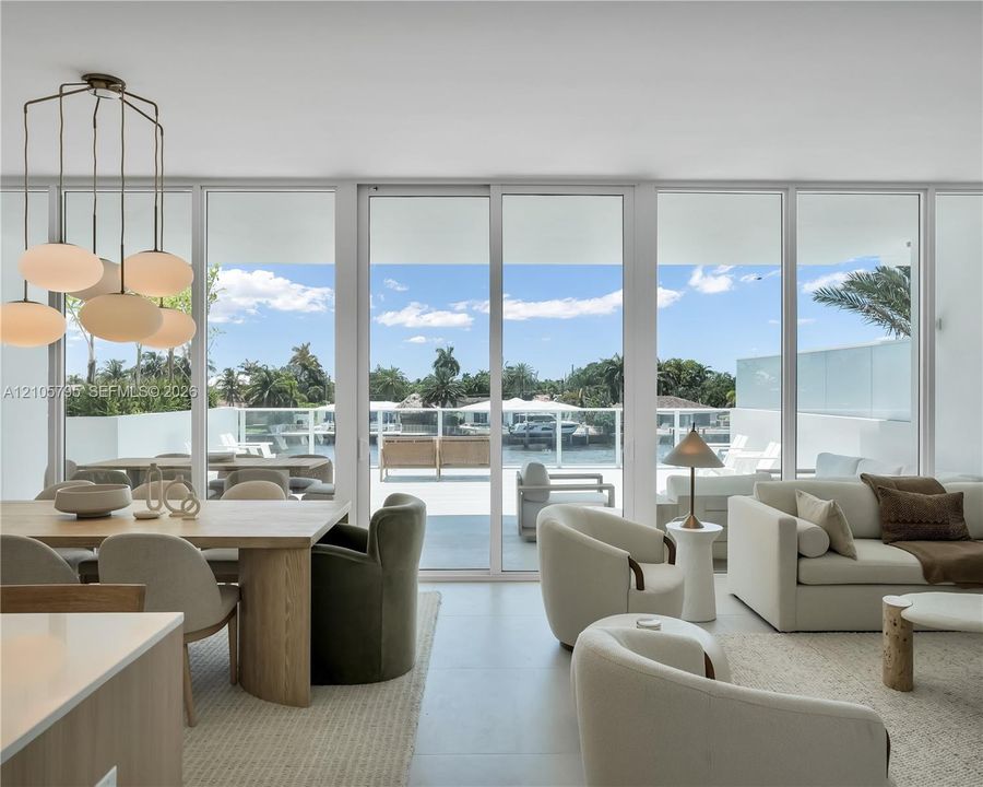 Floor-to-ceiling glass paneling with central sliding doors, expansive balcony, large-format tile flooring, and custom multi-light chandelier fixture