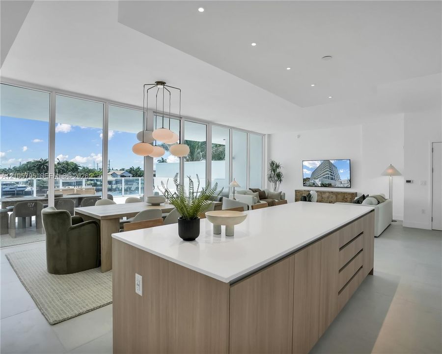 Open-concept interior featuring floor-to-ceiling windows, recessed lighting, expansive center island with solid-surface countertop, and flat-panel wood-finish cabinetry