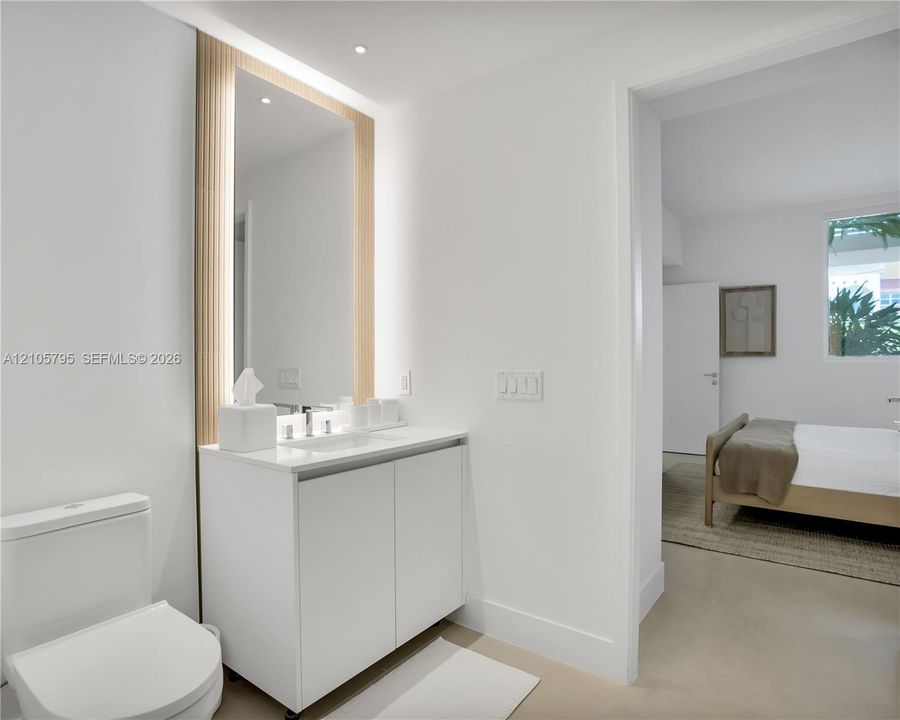 Modern vanity featuring a white cabinet, integrated countertop basin, and polished chrome faucet, accented by a full-height mirror with vertical fluted wood-finish surround and integrated LED lighting