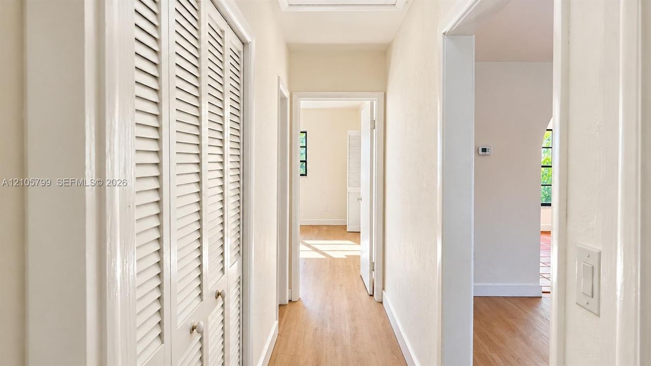 Hallway featuring wood-finish flooring, white louvered-door closets, and arched doorways