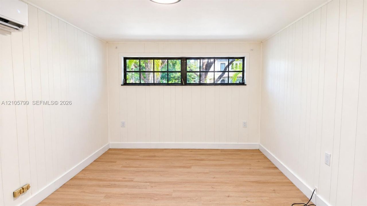Interior space featuring vertical wood-paneled walls, wood-finish flooring, a wall-mounted ductless climate control unit, and a horizontal multi-pane window with a black frame