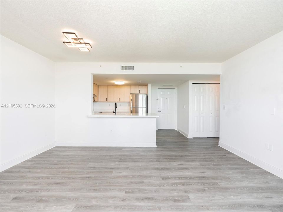 Open-concept floor plan featuring wood-finish flooring, a kitchen pass-through with a solid-surface breakfast bar, light-toned cabinetry, stainless steel appliances, and geometric ceiling lighting