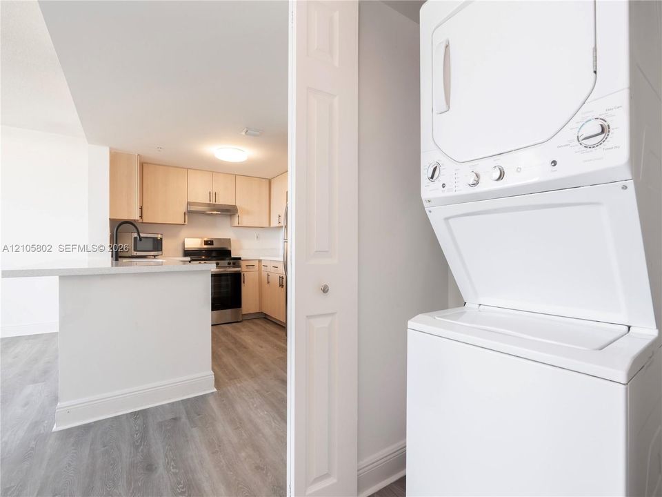 Stacked laundry unit, kitchen featuring flat-panel cabinetry, light-toned countertops, stainless steel gas range, and wood-finish flooring