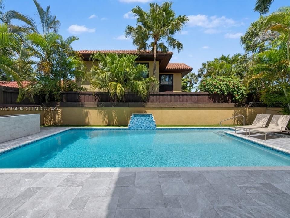 Swimming pool with a tile water feature, stone-finish paver deck, and surrounding privacy fencing
