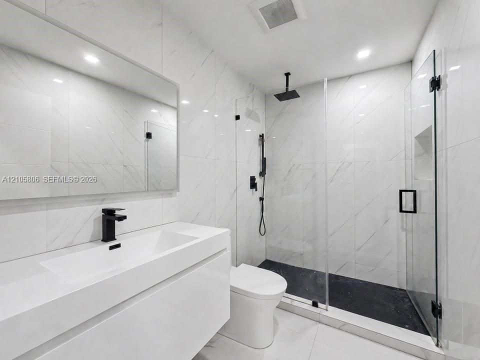 Modern bathroom featuring a wall-mounted vanity, large-format stone-look wall tile, walk-in glass shower enclosure, matte black rainfall shower system, and recessed wall niche