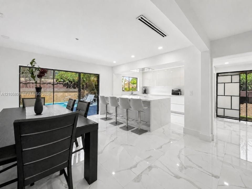 Open-concept kitchen featuring high-gloss cabinetry, a central island with stone-finish countertops, polished large-format tile flooring, and floor-to-ceiling sliding glass doors
