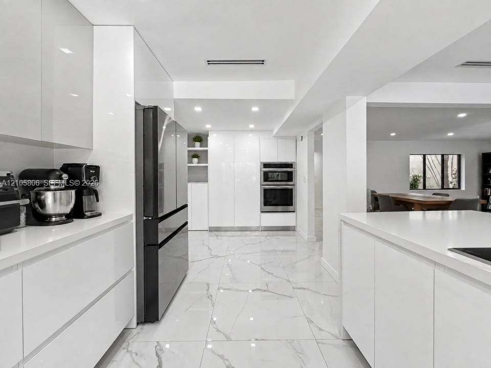 Modern kitchen featuring high-gloss cabinetry, white solid-surface countertops, large-format tile flooring with veining, and stainless steel built-in double wall ovens