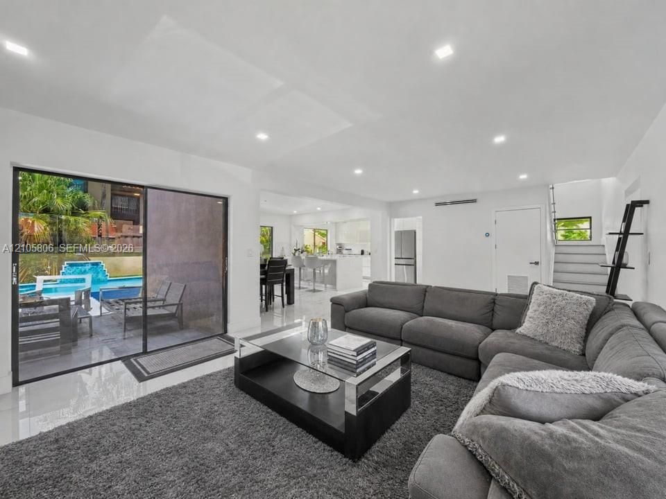 Open-concept living space featuring high-gloss tile flooring, recessed lighting, and large sliding glass doors providing outdoor access to the pool area
