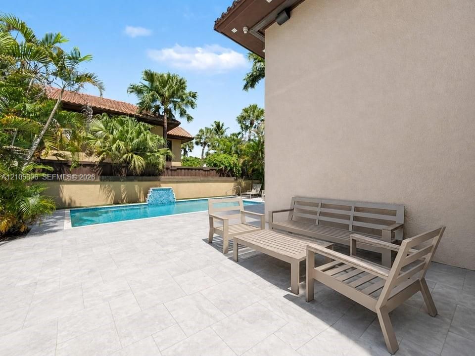 Outdoor living area featuring large-format paver patio, swimming pool with decorative tile water feature, and perimeter masonry wall
