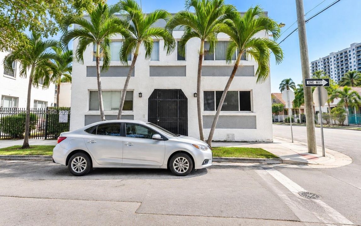 Two-story stucco facade featuring a central arched entryway, metal-framed security gate, dual-tone exterior finish, and large rectangular windows