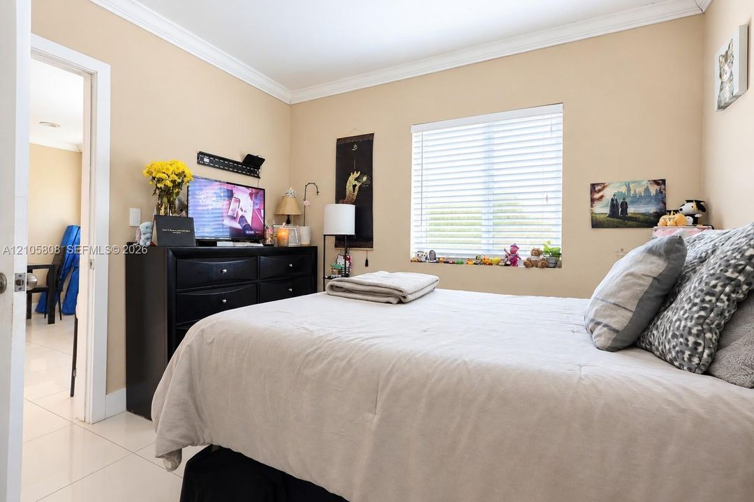 Neutral-toned interior featuring crown molding, polished tile flooring, and a window with installed horizontal blinds