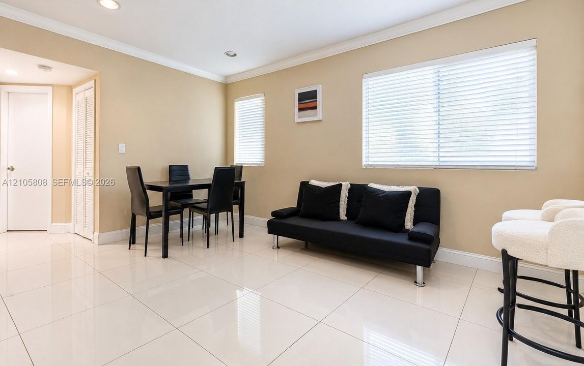 Neutral-toned interior featuring large-format ceramic tile flooring, recessed lighting, crown molding, and multiple windows with horizontal blinds