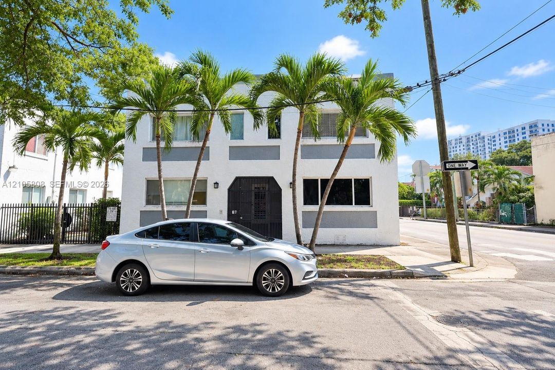 Two-story exterior facade featuring white stucco finish, recessed grey paneling, metal-grille front entryway, and integrated landscaping with mature palm trees