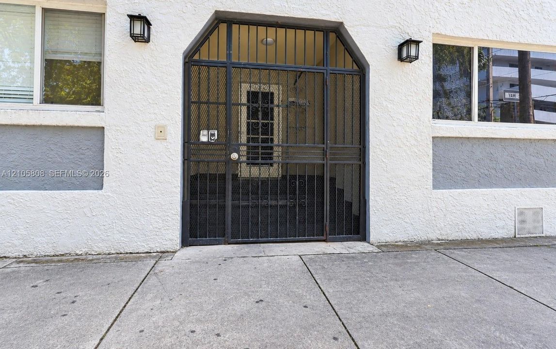 Exterior facade featuring white stucco finish with contrasting gray trim, metal security screen door, and dual wall-mounted outdoor light fixtures
