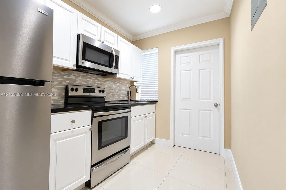 Kitchen featuring white shaker-style cabinetry, stainless steel appliances, dark stone countertops, a mosaic tile backsplash, and light-toned tile flooring