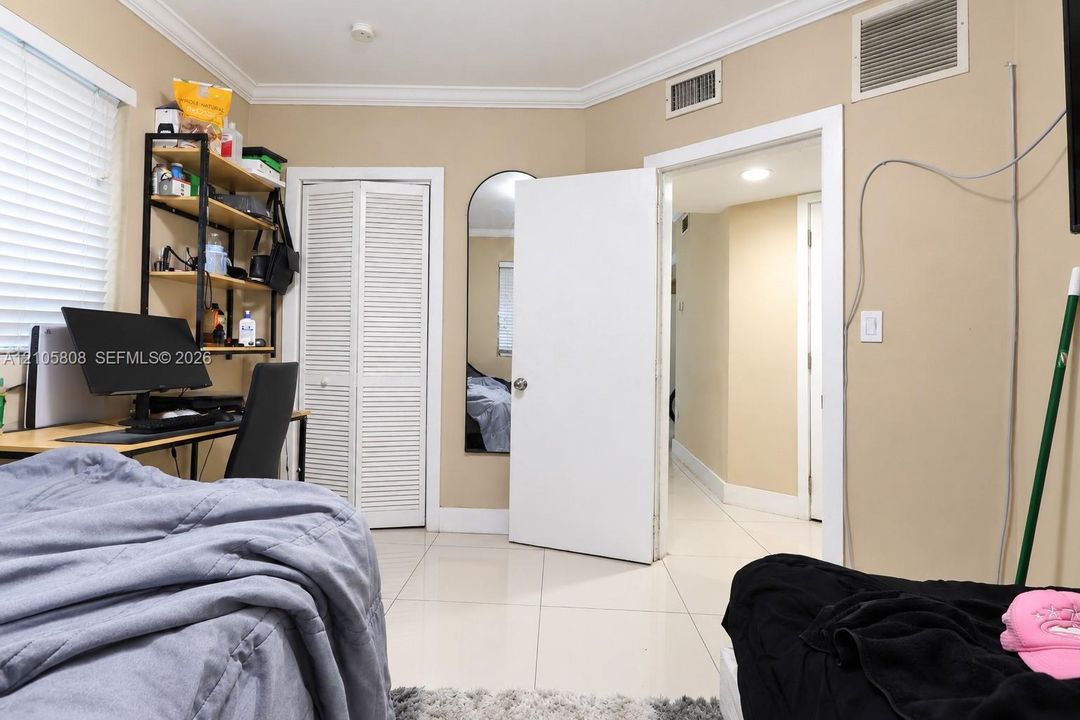 Room featuring large-format tile flooring, white bi-fold closet doors, crown molding, and an arched wall mirror