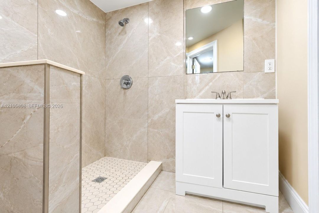 Walk-in shower with floor-to-ceiling stone-finish tile, hexagon mosaic tile flooring, white vanity cabinet, and flush-mount vanity mirror