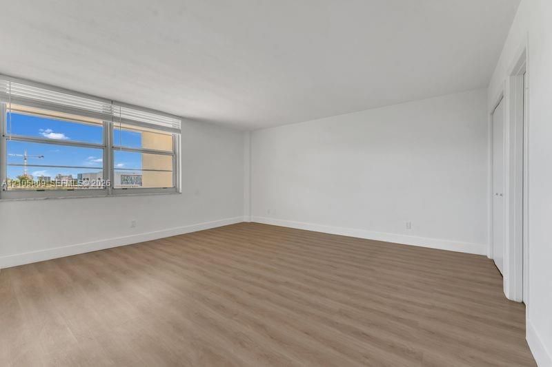 Neutral-toned wood-finish flooring, white walls, and large horizontal sliding windows featuring white blinds