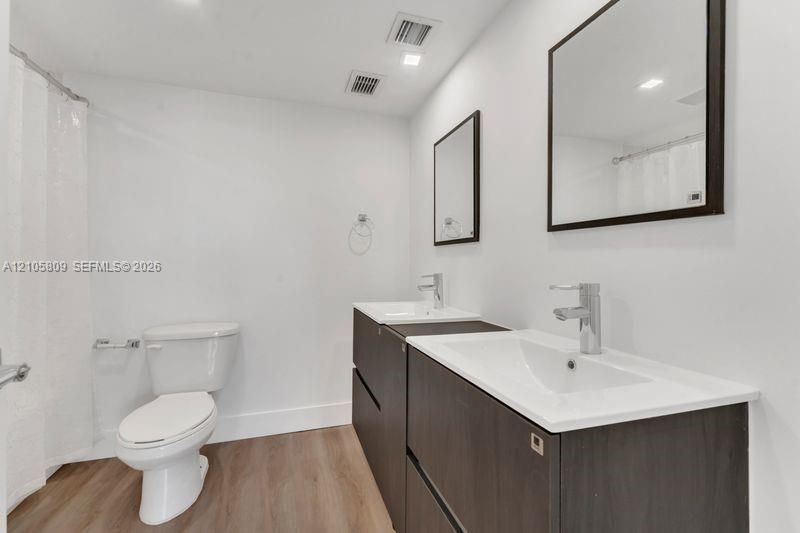 Double vanity featuring dark wood-finish cabinetry, rectangular integrated sinks, chrome fixtures, and wood-finish flooring