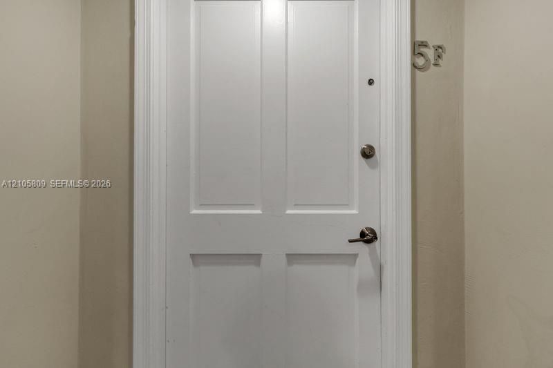 White four-panel door featuring silver-tone lever handle hardware, a security peephole, and integrated metal unit numbering