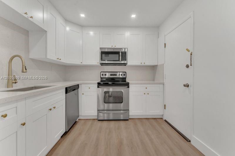 Kitchen featuring white shaker-style cabinetry, quartz countertops, stainless steel appliances, wood-finish flooring, and a high-arch gold-toned faucet