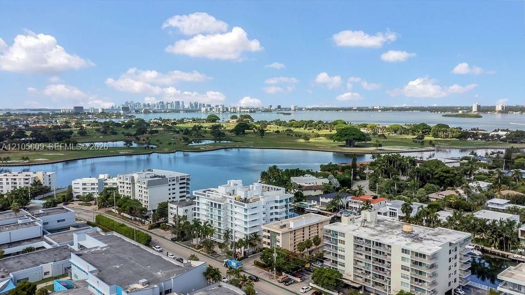 Aerial perspective featuring a waterfront setting, expansive coastal waterway, surrounding golf course, and distant skyline backdrop