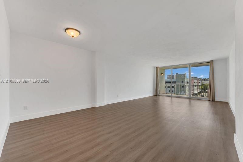 Open floor plan featuring wood-finish flooring, floor-to-ceiling glass doors, and a private balcony with iron railing
