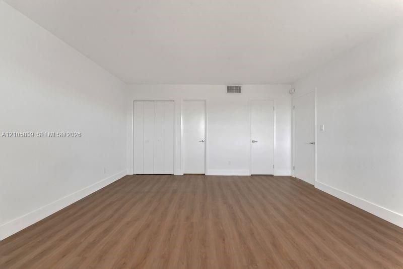 Interior room featuring wood-finish flooring, white walls, and multiple door entries including a double-panel closet