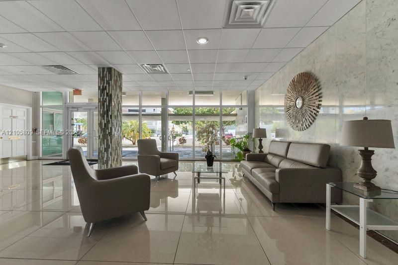 Lobby featuring large-format tile flooring, polished natural stone wall cladding, floor-to-ceiling glass windows, recessed lighting, and a decorative tile-wrapped structural column