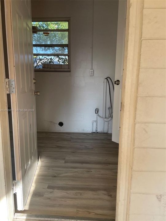 Utility space featuring wood-finish flooring, a horizontal sliding window, and dedicated plumbing connections