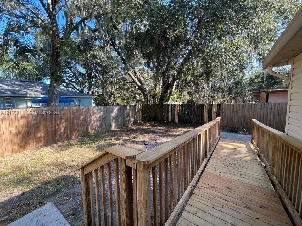Backyard featuring a wood-plank deck, wooden ramp, and perimeter wood privacy fencing set against mature trees