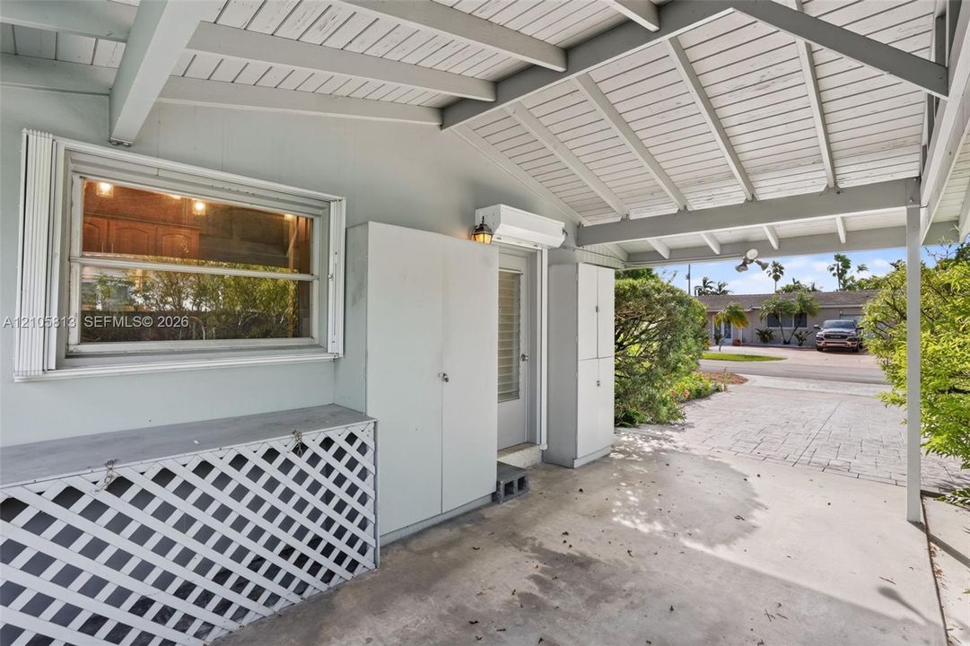 Covered carport featuring a concrete floor, built-in storage cabinetry, decorative lattice screen, exposed beam ceiling, and a concrete driveway