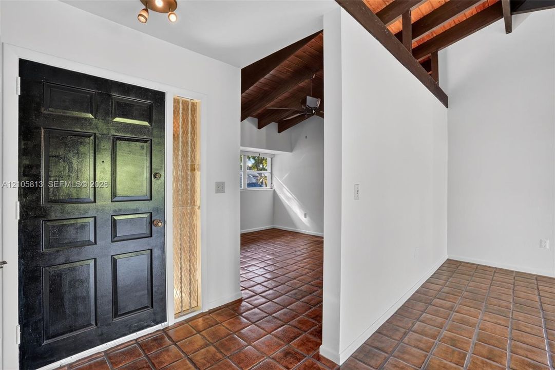 Entryway featuring a paneled front door, vertical glass sidelight, vaulted ceilings with exposed wood beams, and ceramic tile flooring