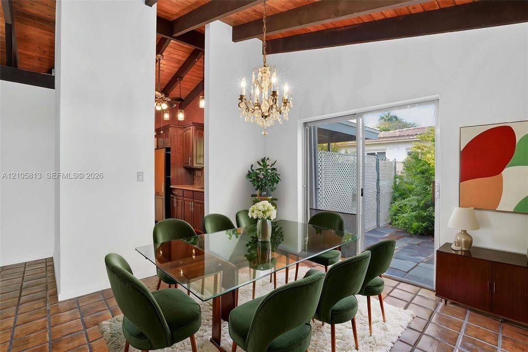 Vaulted ceilings with exposed timber beams, ceramic tile flooring, a multi-light crystal chandelier, and sliding glass doors to the exterior patio