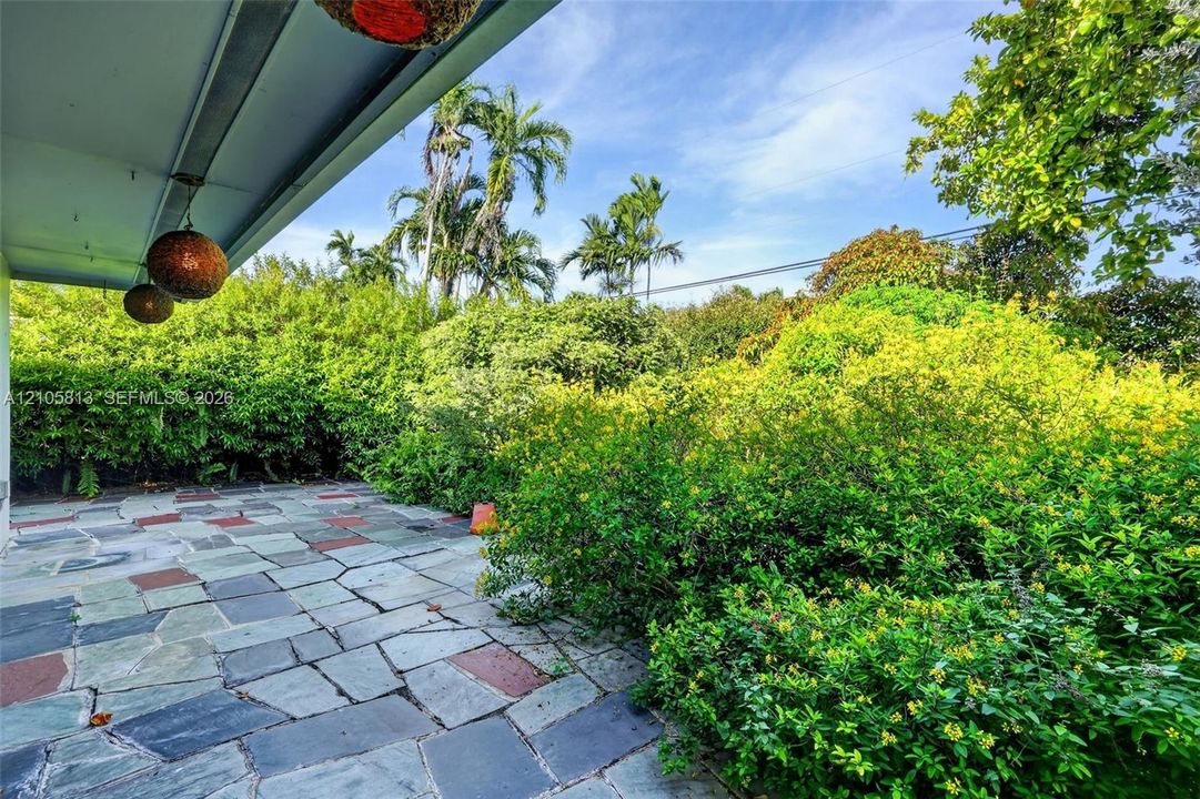 Covered outdoor patio featuring multicolored flagstone paving, integrated spherical pendant lighting, and mature perimeter landscaping