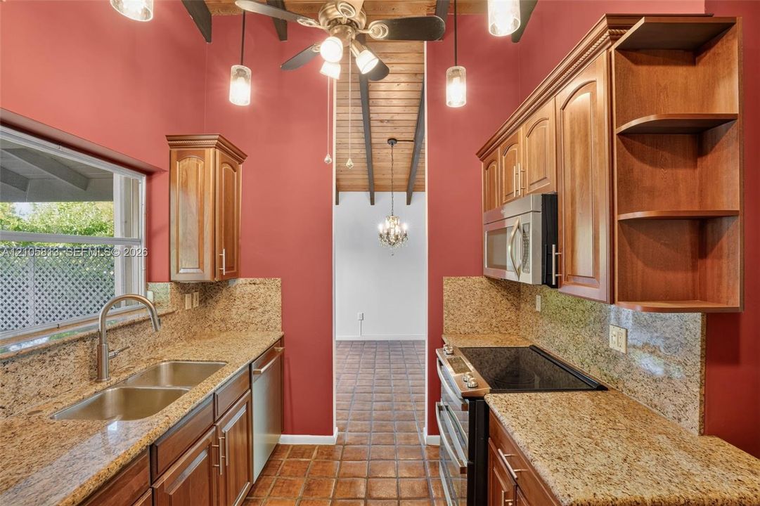Kitchen featuring wood cabinetry, stone-surface countertops, tile flooring, and a vaulted ceiling with exposed beams