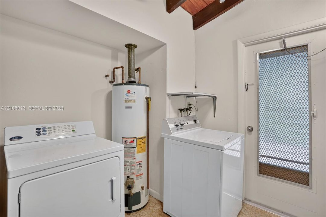 Utility space featuring exposed wood-beam ceiling, water heater, and exterior door with integrated security screen
