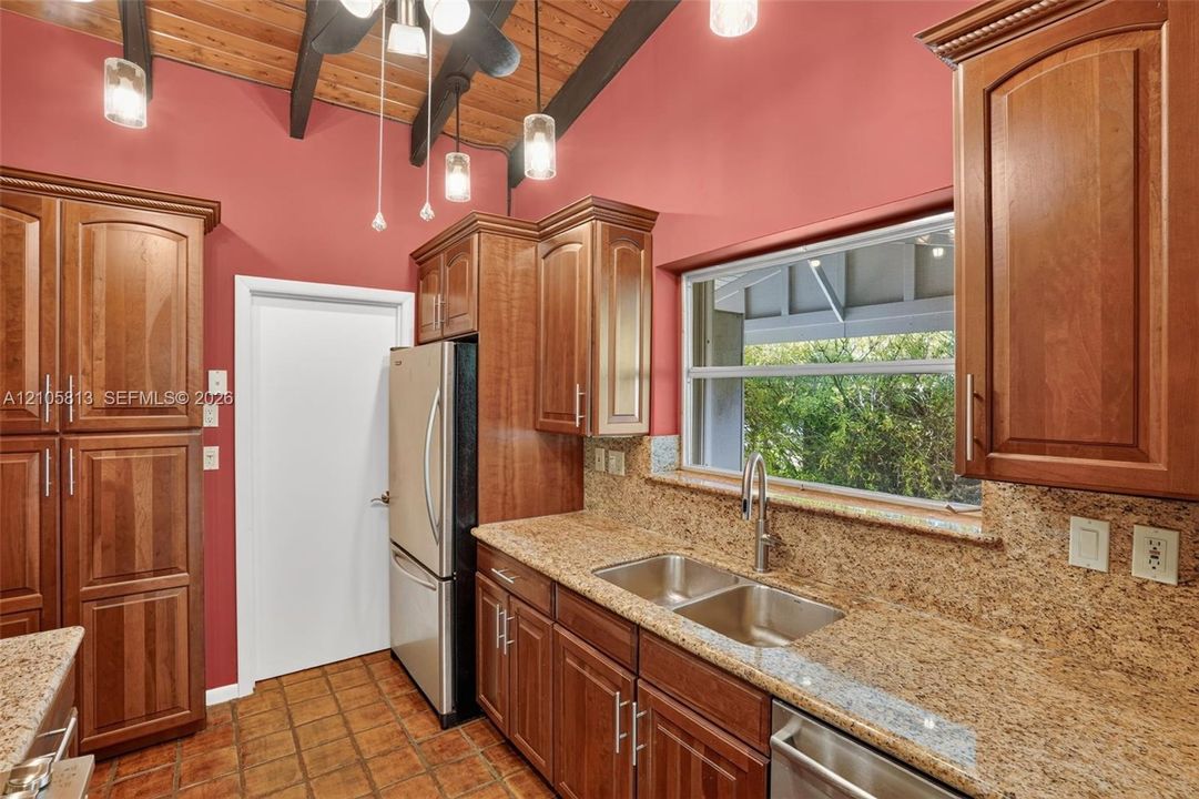 Kitchen featuring wood cabinetry, stone countertops, stainless steel appliances, tile flooring, and a vaulted ceiling with exposed wood beams