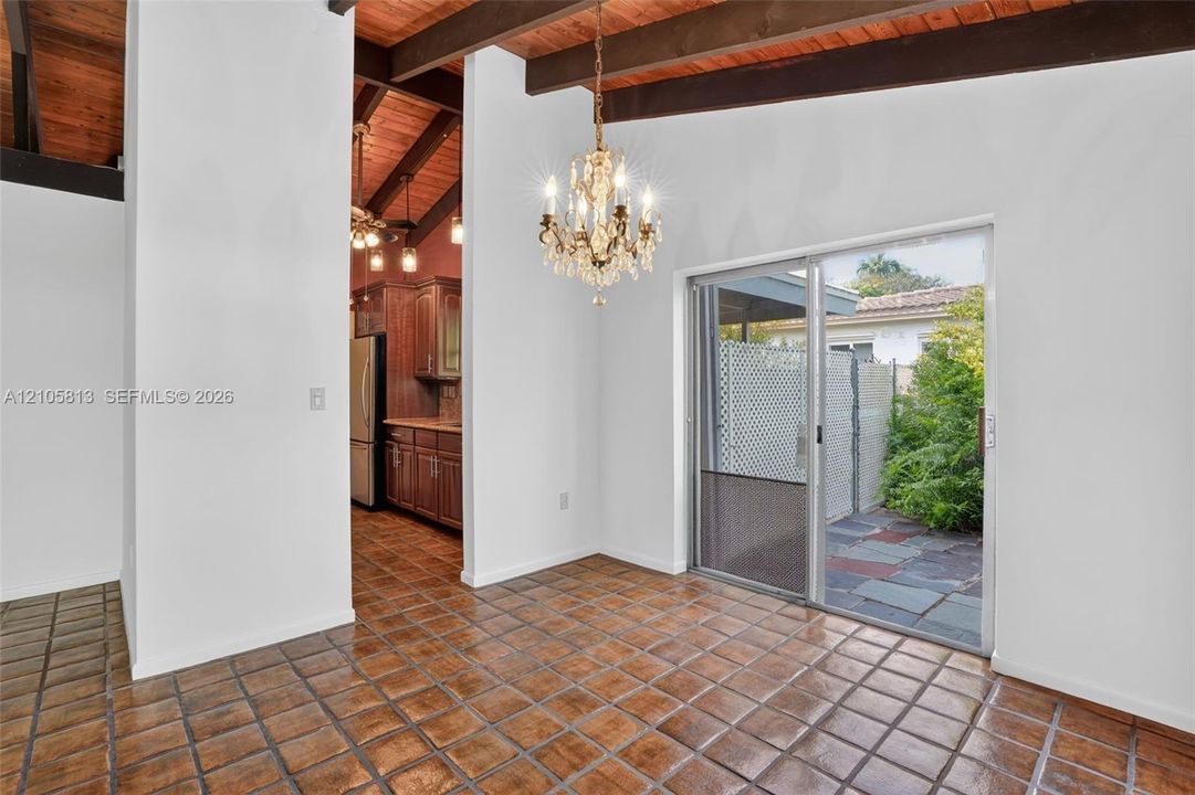 Exposed wood beam ceilings, square tile flooring, multi-light chandelier, and glass sliding doors