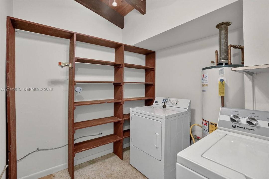 Utility space featuring built-in wooden shelving, exposed ceiling beams, and a dedicated water heater