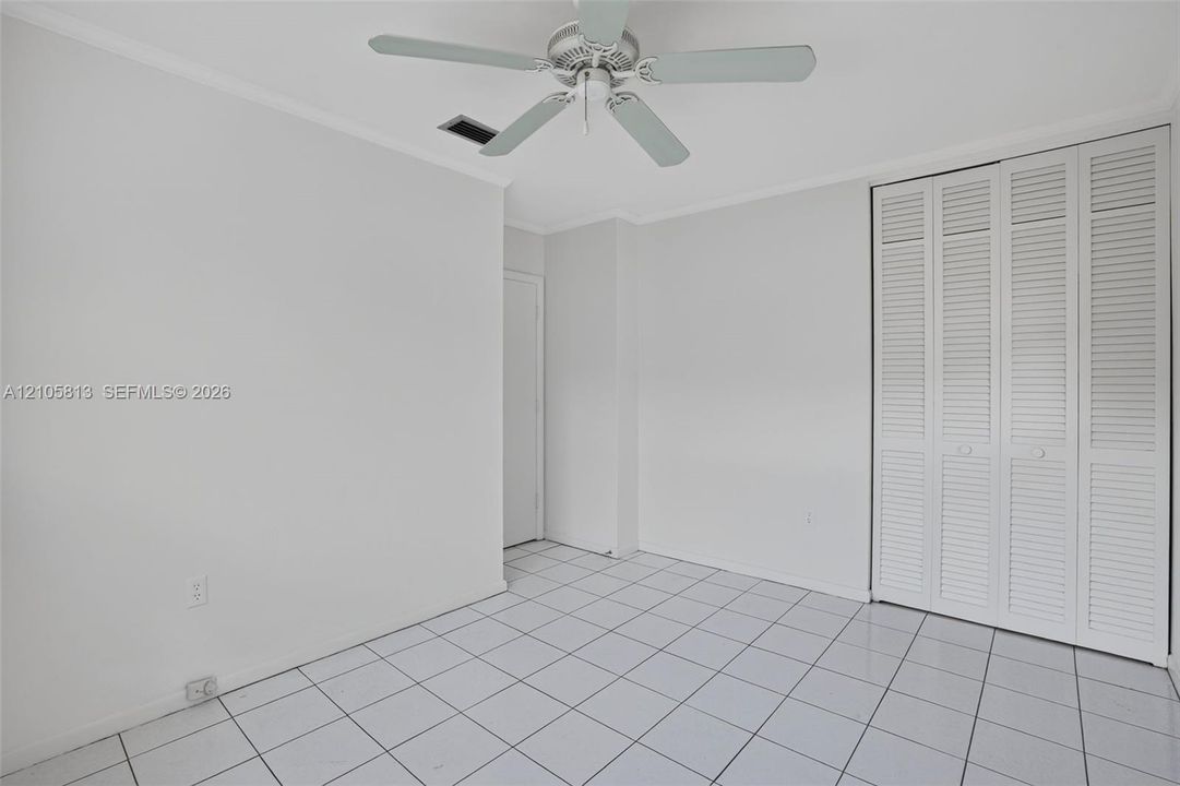 Interior space featuring light-colored tile flooring, white bi-fold closet doors, and a ceiling fan