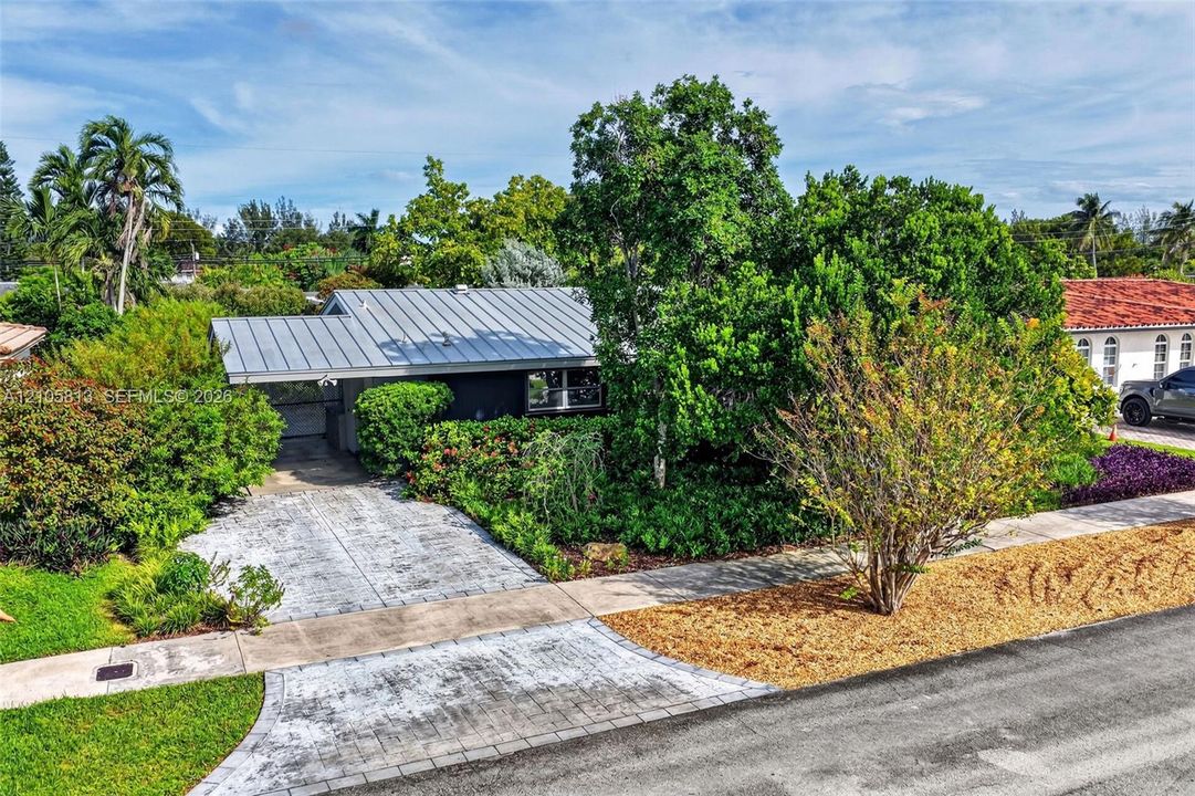 Single-story residence featuring a metal roof, paved driveway, and mature landscaping
