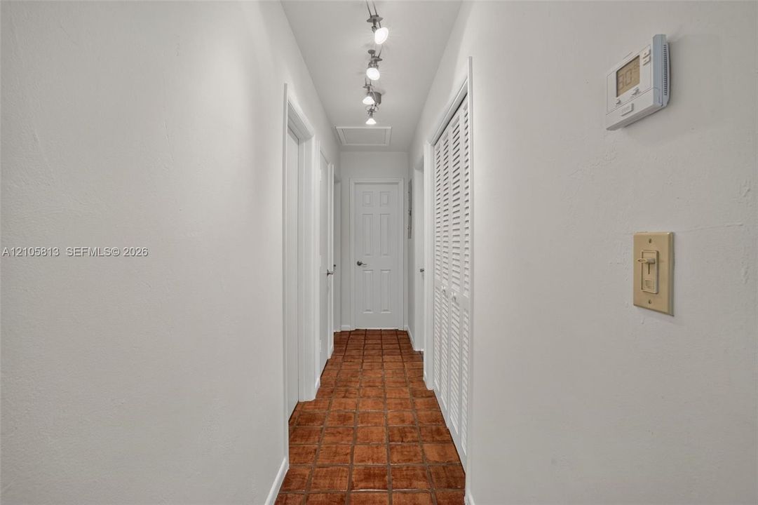 Interior hallway featuring terra cotta tile flooring, multi-panel doors, louvered closet doors, and adjustable track lighting