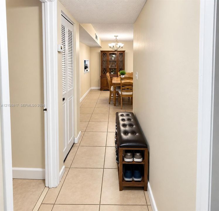 Hallway featuring neutral-toned tile flooring, louvered closet doors, and a recessed wall niche