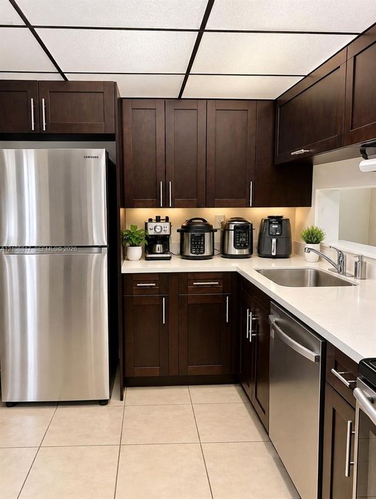 Kitchen featuring dark-finish cabinetry, white countertops, stainless steel appliances, a stainless steel undermount sink, and tile flooring