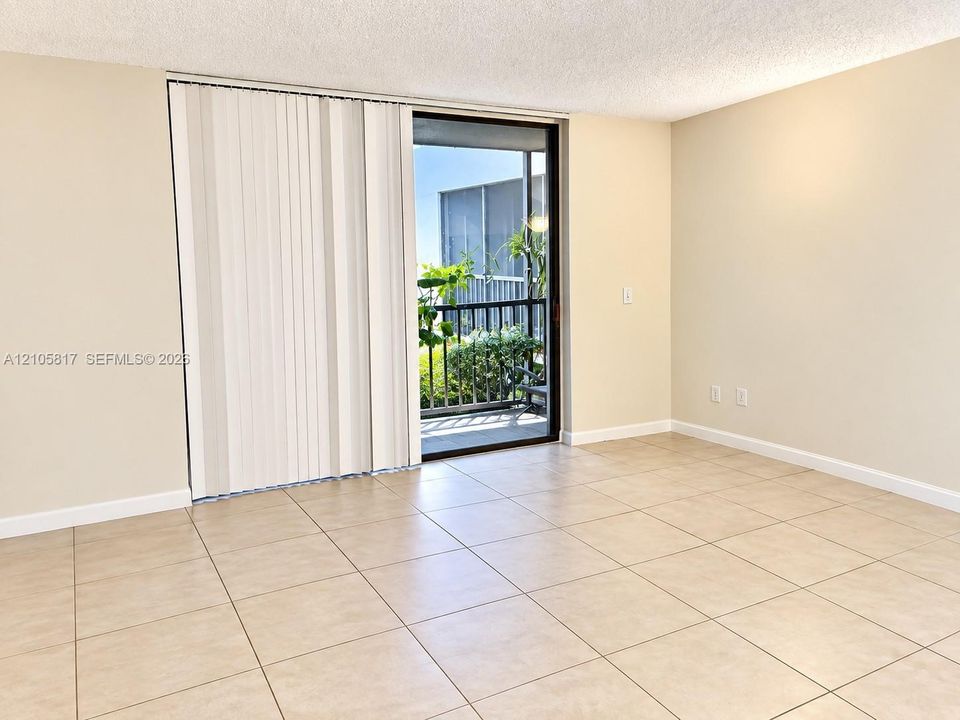 Large-format neutral floor tiling, sliding glass door with vertical blinds, and attached balcony with metal railings