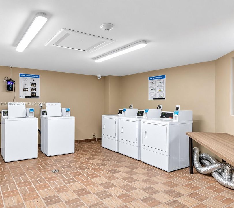Laundry facility featuring tile flooring, linear LED lighting, and multi-unit laundry appliances with a built-in folding counter
